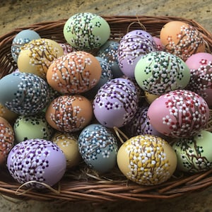 Könnte beinhalten: Ein Korb voller handbemalter Ostereier. Die Eier sind mit einem Blumenmuster in verschiedenen Farben verziert, darunter Rosa, Lila, Grün, Gelb und Orange.