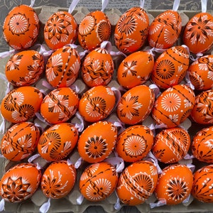 Peut inclure: Une collection de 27 œufs de Pâques orange décorés de motifs blancs et noirs. Les œufs sont disposés dans un carton.