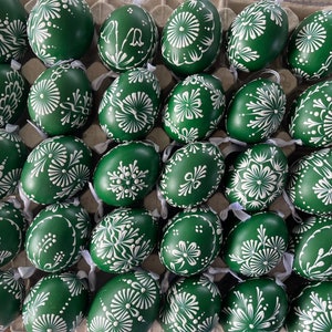 Könnte beinhalten: Eine Sammlung grüner Ostereier, die mit weißen Blumenmustern verziert sind. Die Eier sind in einem Karton angeordnet.
