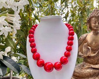 Può includere: Una collana di perline di legno rosso su un busto di manichino bianco. La collana è composta da grandi perline rotonde.