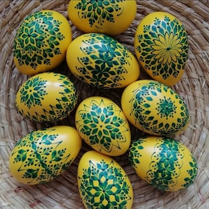 Könnte beinhalten: Zehn gelbe Ostereier, die mit grünen Blumenmustern verziert sind. Die Eier sind in einem Korb angeordnet.
