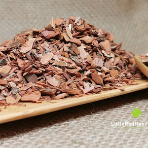 May include: A pile of dried, reddish-brown bark chips on a wooden surface. The bark is broken into small pieces and has a rough texture.