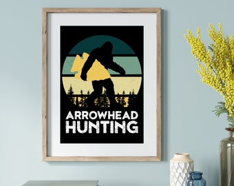 May include: A black and white graphic design featuring a silhouette of Bigfoot carrying an arrowhead in front of a retro sunset with the text "Arrowhead Hunting".