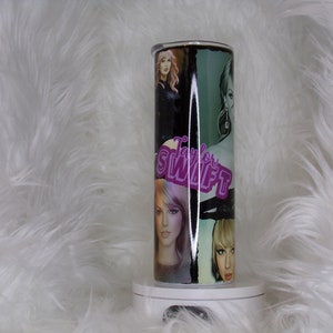 May include: A stainless steel tumbler with a black and green design featuring multiple images of Taylor Swift. The tumbler has a pink "Taylor Swift" logo.
