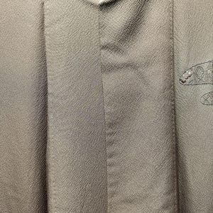 K&ouml;nnte beinhalten: Ein grauer Kimono mit einem dezenten, strukturierten Muster. Der Kimono ist in der H&auml;lfte gefaltet und die R&uuml;ckseite ist sichtbar. Der Kimono hat ein dekoratives Design auf der R&uuml;ckseite.