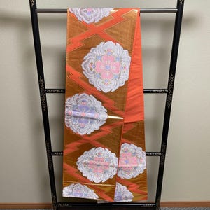 May include: A handmade wooden sign with the text "Welcome" in a playful font. The sign is painted white with a distressed finish, and features a decorative floral design in shades of pink and green. It is designed for indoor or outdoor use.