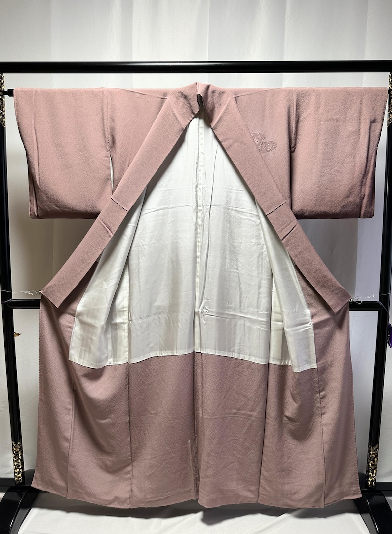 K&ouml;nnte beinhalten: Ein mauvefarbener Kimono mit wei&szlig;em Futter und einem kleinen gestickten Schmetterlingsmuster auf der R&uuml;ckseite.