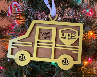 Op de afbeelding: Een gele houten ornament in de vorm van een UPS-bezorgwagen met de woorden "Thank You" en "ups" aan de zijkant. De ornament heeft het nummer "20" op elk wiel.