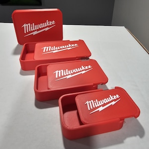 May include: Four red storage containers with white "Milwaukee" logos. The containers are rectangular with rounded corners and lids. The lids are open on three of the containers, revealing the interior.