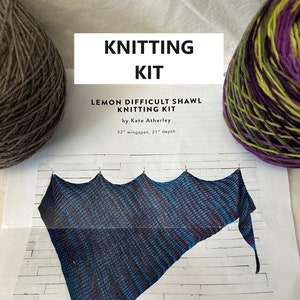 May include: Knitting kit for a lemon difficult shawl by Kate Atherley. The kit includes two skeins of yarn, one in a dark grey color and the other in a purple, green, and yellow color. The finished shawl is shown in the image and measures 52 inches in wingspan and 21 inches in depth.