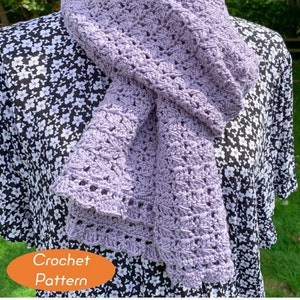May include: A lavender crochet scarf with a delicate openwork pattern. The scarf is displayed on a mannequin wearing a black and white floral dress. The text "Crochet Pattern" is visible in the lower left corner of the image.