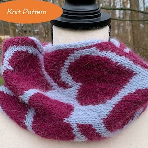 May include: A knitted cowl with a geometric pattern in shades of purple and light blue. The cowl is made with a fuzzy yarn and has a soft, textured look.