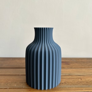 May include: A dark blue ceramic vase with a fluted design. The vase has a rounded base and a narrow opening.