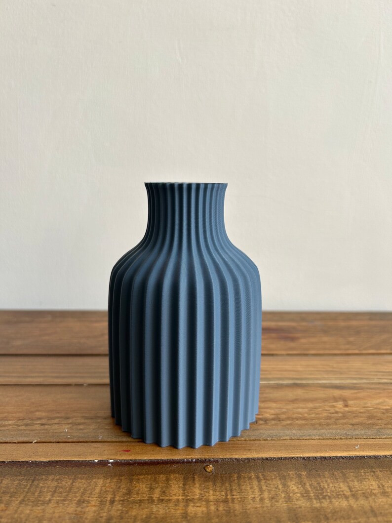 May include: A dark blue ceramic vase with a fluted design. The vase has a rounded base and a narrow opening.