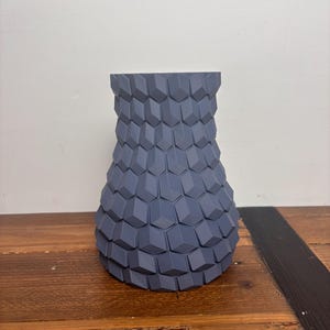Op de afbeelding: Een grijze keramische vaas met een geometrisch patroon. De vaas heeft een brede basis en een smalle hals.
