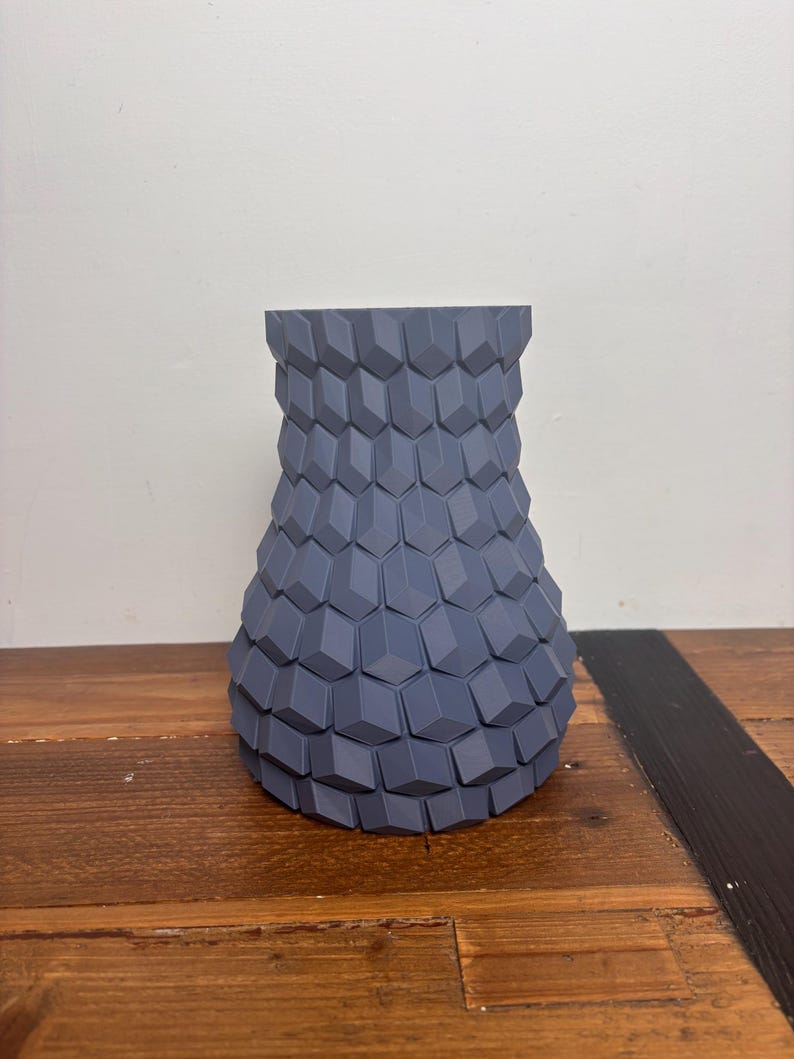 Op de afbeelding: Een grijze keramische vaas met een geometrisch patroon. De vaas heeft een brede basis en een smalle hals.
