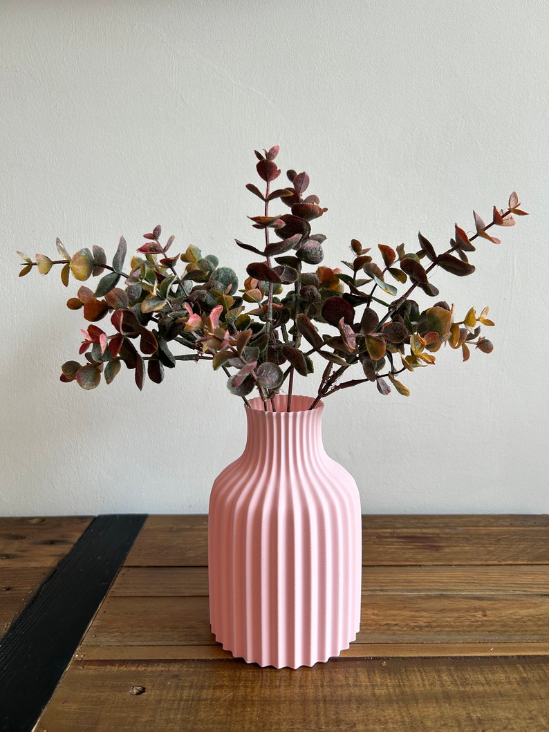 May include: A pink ceramic vase with a ribbed design, holding a bouquet of dried eucalyptus branches.