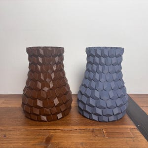 Op de afbeelding: Twee keramische vazen met een geometrisch patroon. De vaas links is bruin en de vaas rechts is blauw.