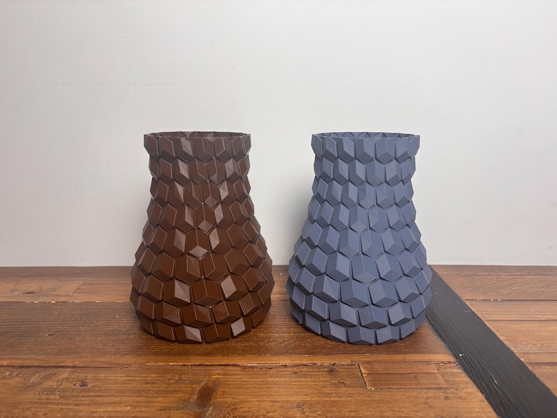 Op de afbeelding: Twee keramische vazen met een geometrisch patroon. De vaas links is bruin en de vaas rechts is blauw.