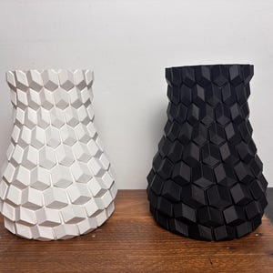 Op de afbeelding: Twee keramische vazen met een geometrisch patroon. De ene vaas is wit en de andere is zwart.