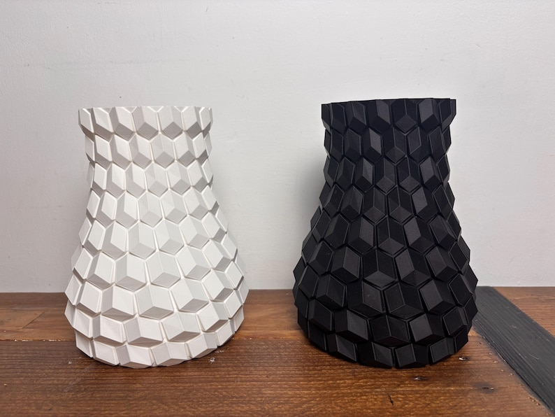 Op de afbeelding: Twee keramische vazen met een geometrisch patroon. De ene vaas is wit en de andere is zwart.