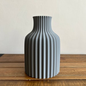 May include: A gray ceramic vase with a ribbed design. The vase has a rounded body and a narrow neck.
