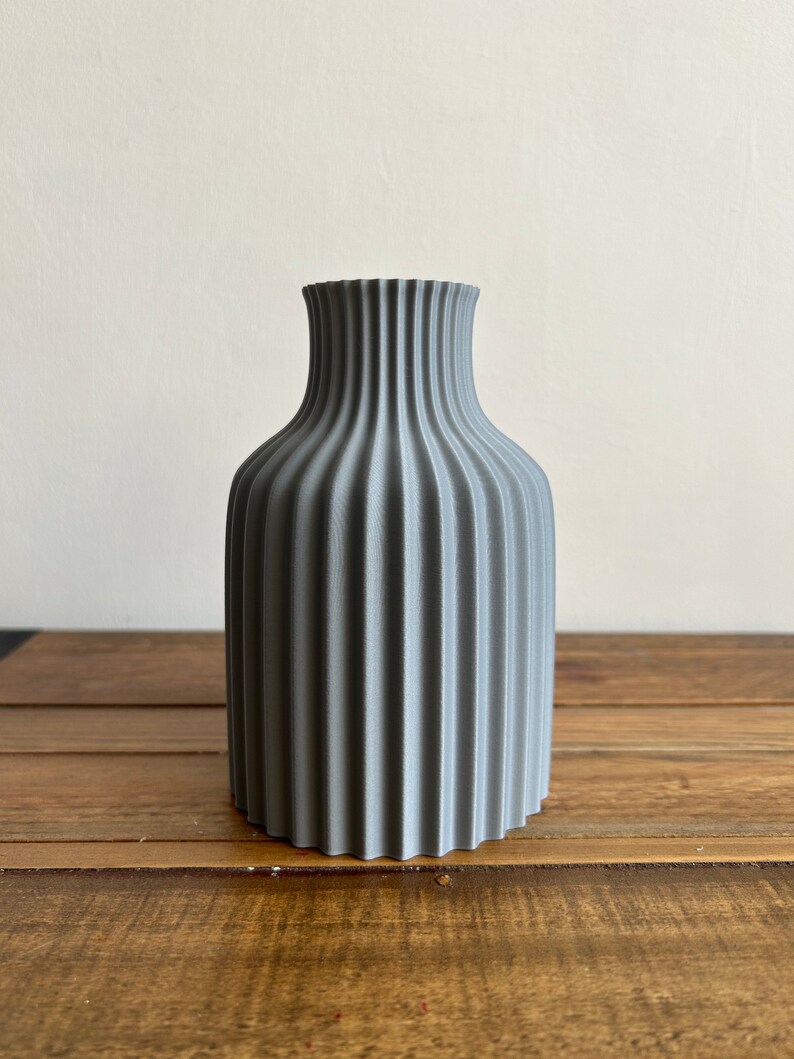 May include: A gray ceramic vase with a ribbed design. The vase has a rounded body and a narrow neck.