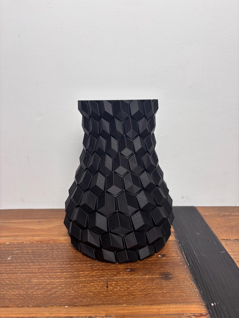 Op de afbeelding: Een zwarte keramische vaas met een geometrisch patroon. De vaas is gemaakt van een getextureerd materiaal en heeft een brede basis en een smalle hals.