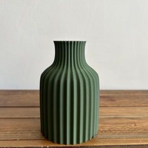 May include: A dark green ceramic vase with a ribbed design. The vase is about 6 inches tall and has a narrow opening.