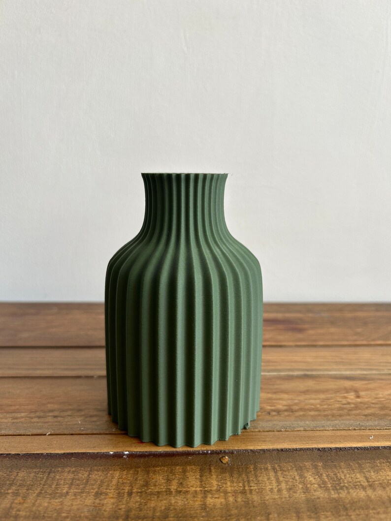 May include: A dark green ceramic vase with a ribbed design. The vase is about 6 inches tall and has a narrow opening.