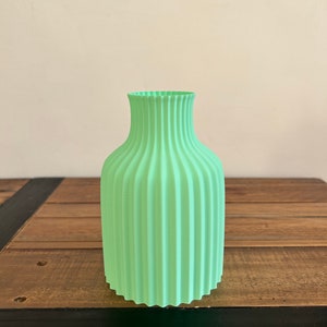May include: A light green ceramic vase with a ribbed design. The vase is sitting on a wooden surface.