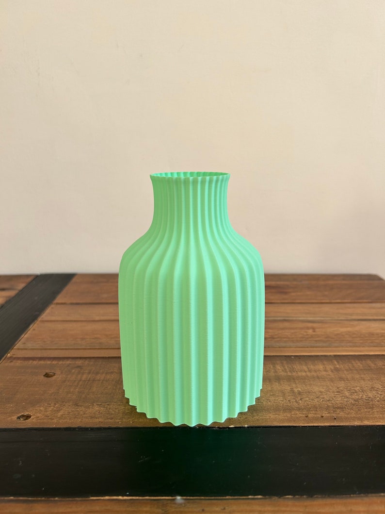 May include: A light green ceramic vase with a ribbed design. The vase is sitting on a wooden surface.