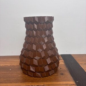Op de afbeelding: Een bruine keramische vaas met een geometrisch patroon. De vaas is gemaakt van een getextureerd materiaal en heeft een brede basis en een smalle hals.