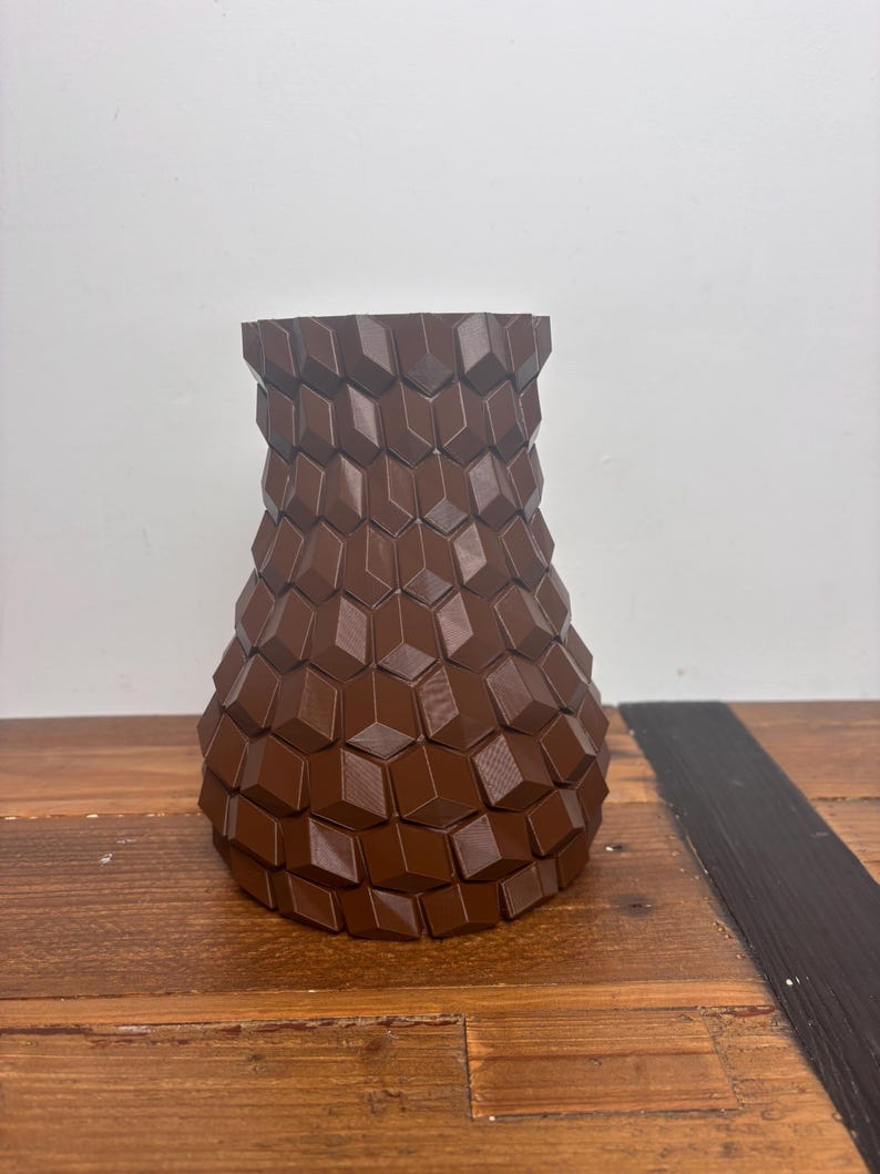 Op de afbeelding: Een bruine keramische vaas met een geometrisch patroon. De vaas is gemaakt van een getextureerd materiaal en heeft een brede basis en een smalle hals.