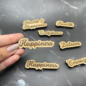 May include: Wooden plaques with inspirational words like "Happiness", "Health", "Believe", "Confidence", and "Courage" engraved in a cursive font.