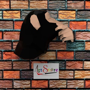 May include: A black chimpanzee head and hand sculpture emerging from a brick wall. The sculpture is set against a backdrop of a multi-colored brick wall. The image includes the text "Art Store" in a colorful, stylized font.