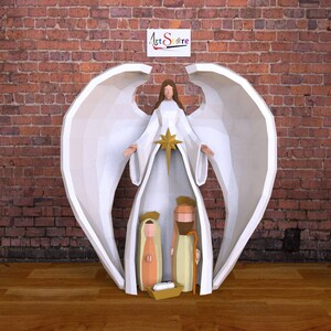 Puede incluir: Un ángel de papel blanco con alas grandes se encuentra sobre un pesebre. El ángel sostiene una estrella y el pesebre incluye un pesebre, un bebé, María y José.