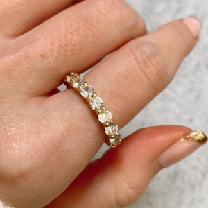 Op de afbeelding: Een gouden ring met een rij van heldere ronde stenen.