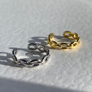 Puede incluir: Dos anillos ajustables de eslabones de cadena, uno plateado y otro dorado. Los anillos son de metal y tienen un diseño simple y moderno.