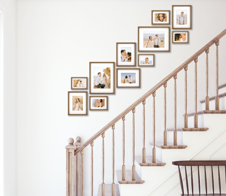 Puede incluir: Una colecci&oacute;n de fotograf&iacute;as enmarcadas de varios tama&ntilde;os, dispuestas en una pared blanca sobre una escalera. Los marcos son de color marr&oacute;n c&aacute;lido y las fotos muestran a personas en diversos entornos. La escalera tiene una barandilla de madera y escalones blancos.