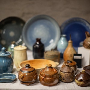 May include: A collection of ceramic pottery in various shapes and sizes, including bowls, jars, and pitchers. The pottery is decorated with different colors and patterns, including blue, brown, and white.