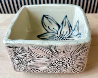 May include: A white ceramic square dish with a blue floral design inside and a pink floral design on the outside.