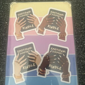Pode incluir: Capa Kindle com um fundo listrado colorido. A capa apresenta quatro adesivos com o texto "EMOTIONAL SUPPORT" e "KINDLE". Os adesivos retratam m&atilde;os adornadas com joias de ouro.