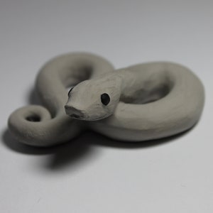 May include: A small, gray, ceramic snake figurine with black eyes. The snake is curled up in a coil.