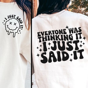 May include: White sweatshirt with a black graphic on the front that says "I just said it!" and a melting smiley face. The back of the sweatshirt has a black graphic that says "Everyone was thinking it I just said it!" with stars around the text.