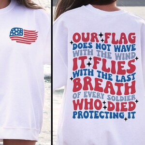 May include: White sweatshirt with a red, white, and blue American flag on the front and a patriotic message on the back that reads "OUR FLAG DOES NOT WAVE WITH THE WIND IT FLIES WITH THE LAST BREATH OF EVERY SOLDIER WHO DIED PROTECTING IT".