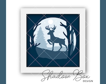 Puede incluir: Un diseño de caja de sombra azul y blanca con la silueta de un ciervo de pie en un bosque con luna llena en el fondo. El texto "Shadow Box Design" está en la parte inferior de la imagen.