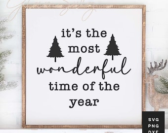 May include: A white wooden sign with black text that reads "it's the most wonderful time of the year" with two stylised pine trees on either side of the text.