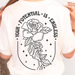 May include: White t-shirt with a black graphic of a rose and a hand holding the stem. The text "Your Potential Is Endless" is written in a circle around the rose.