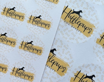May include: Close-up of several round stickers with a yellow background and a black silhouette of a dog running. The text "Hufflepups Dog Bakery" is written in black cursive on the stickers.